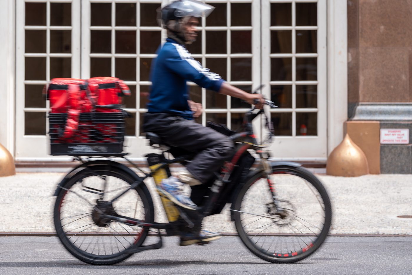 A courier riding an e-bike with delivery bags on the rear rack